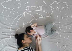 femme et bébé allongé abrités d'une pluie dessinée par un parapluie dessiné