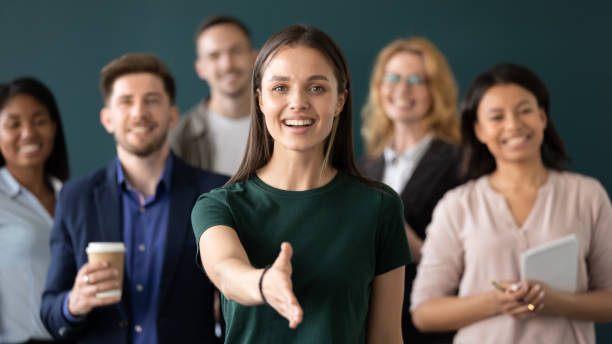 Une femme salariée tend la main pour souhaiter la bienvenue. Son équipe est en arrière plan.